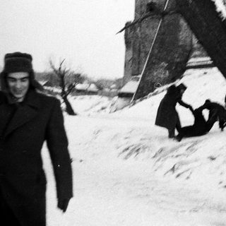 Man stands near children playing in snowy landscape.