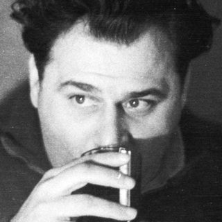 Man holding a drink, smoking, in a dimly lit room.