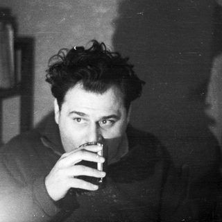 Man holding a drink, smoking, in a dimly lit room.