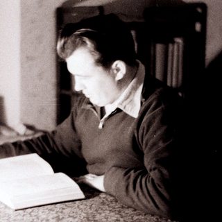 Here's a brief summary of the image: Man reading a large book at a table.