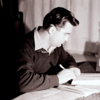 Man writing at a desk, with books and a photo.