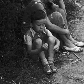 A woman and child sit near foliage, appearing distressed.