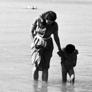 A woman and child stand in shallow water.