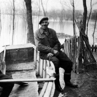 Two men sit in a boat in a flooded landscape.