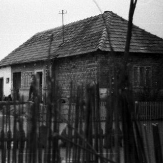 Old, weathered house with a shingled roof and fence.