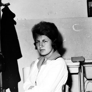 Here's a brief summary of the image: Woman seated in a simple, utilitarian room.
