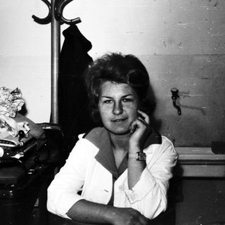 Woman sits in a room with luggage and furniture.