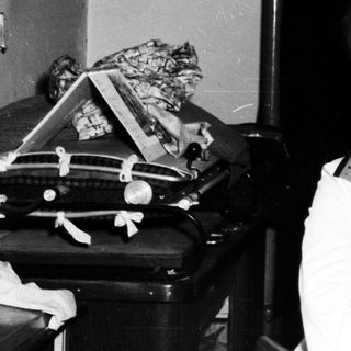 Woman sits near a sink and trunk, looking at camera.