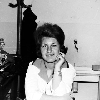 Woman sits near a sink and trunk, looking at camera.