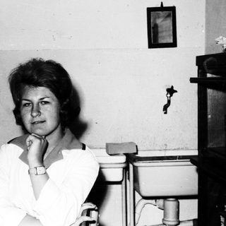 Here's a brief summary of the image: Woman with short hair sits in a room with vintage items.