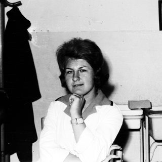 Here's a brief summary of the image: Woman with short hair sits in a room with vintage items.