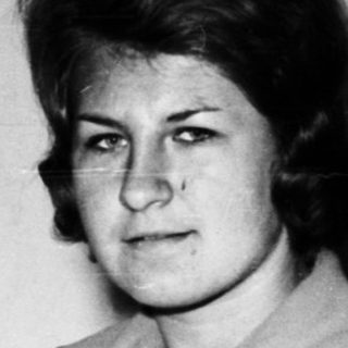 Woman seated in a restroom, looking directly at the camera.
