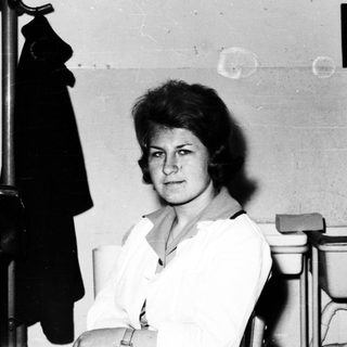 Woman seated in a restroom, looking directly at the camera.