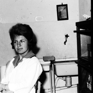 Woman seated in a room with a sink and shelves.