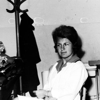Woman seated in a room with a sink and shelves.