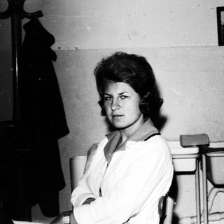 Woman sits in a room with a sink and coat rack.