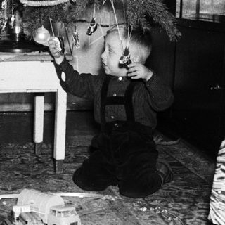 Boy plays with a toy train set near a Christmas tree.