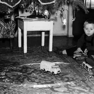 Boy plays with toy train set near Christmas tree.