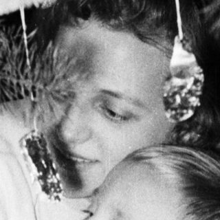 Boy in overalls sits near a decorated Christmas tree.