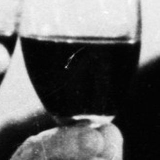 Two men in suits toast with glasses of red wine.