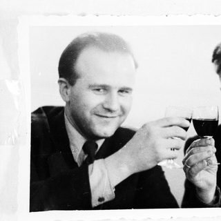 Two men in suits toast with glasses of red wine.