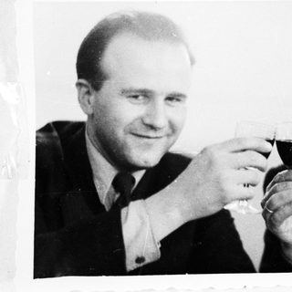 Two men in suits toast with glasses of red wine.