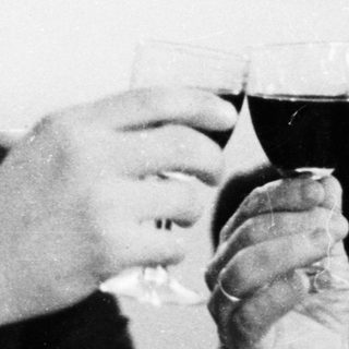 Two men in suits toast with glasses of red wine.