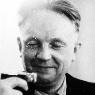Man raises a glass, smiling in a black and white photo.