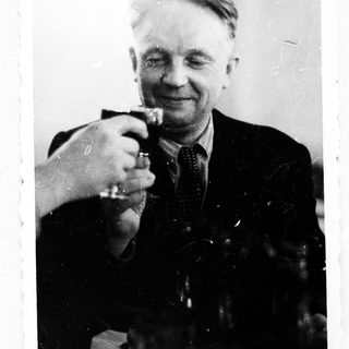 Man raises a glass, smiling in a black and white photo.