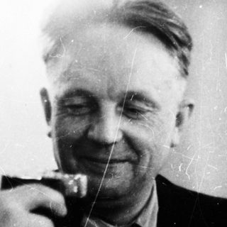 Here's a brief summary of the image: Man in suit raising a glass, appearing to be toasting.