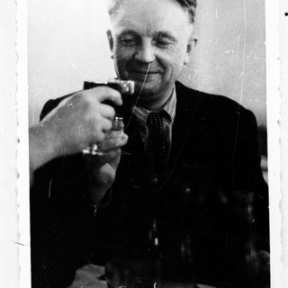 Here's a brief summary of the image: Man in suit raising a glass, appearing to be toasting.