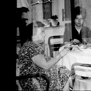 Here's a brief summary of the image: Family gathers around a table for a meal.