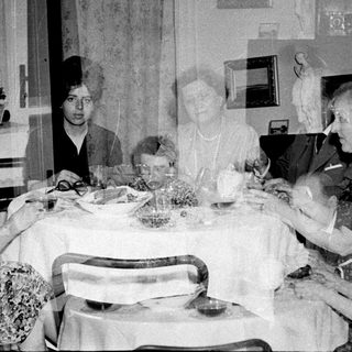 Here's a brief summary of the image: Family gathers around a table for a meal.