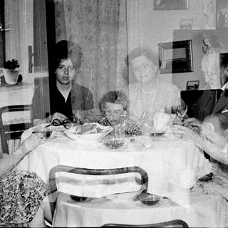 Here's a brief summary of the image: Family gathers around a table for a meal.