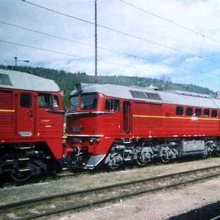 Red electric locomotive sits on tracks under a cloudy sky.