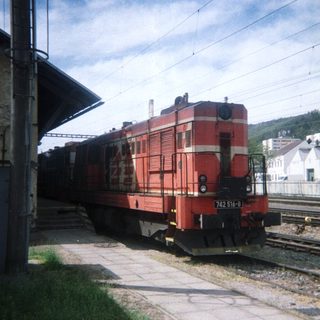 Red locomotive stands at a platform beside train tracks.