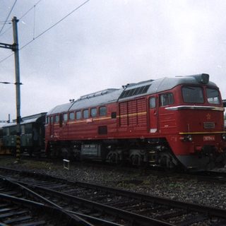Red locomotive sits on tracks with train cars nearby.