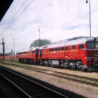 Red locomotive travels along train tracks on a sunny day.