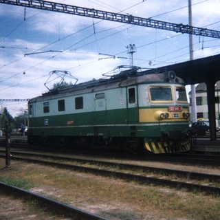 Green electric locomotive sits on railway tracks at a station.