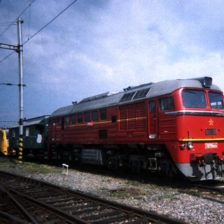 Red locomotive stands on tracks near a building.