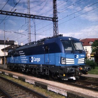Blue freight locomotive stands on railway tracks near a station.