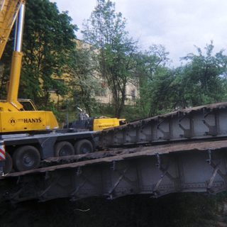 Crane moves a metal bridge section over a waterway.
