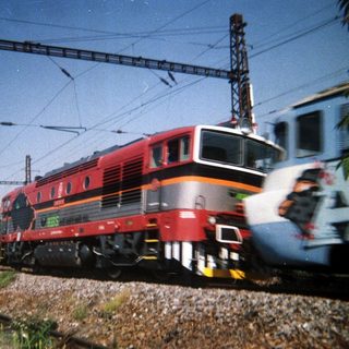Red locomotive sits on tracks with overhead electric lines.