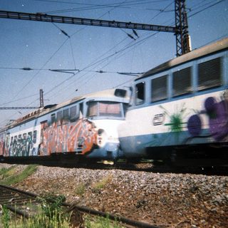 Graffiti-covered train traveling on tracks under power lines.