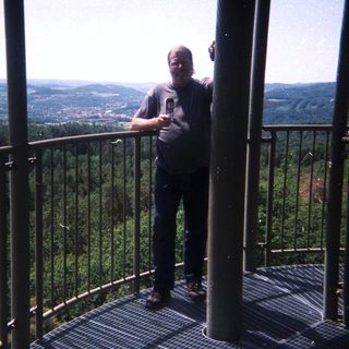Man stands on a tower overlooking a forested landscape.