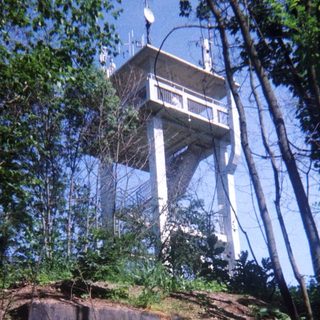 A tall communications tower sits atop a wooded hillside.