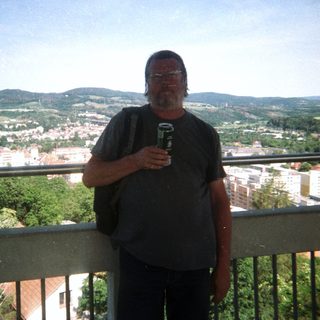Man stands on a balcony overlooking a town and hills.