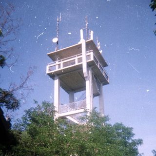 Concrete observation tower stands above greenery and a fence.