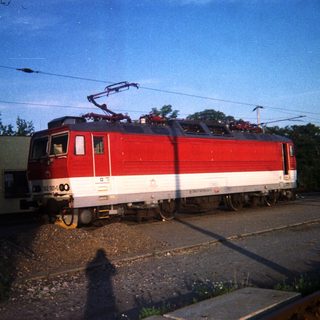 Red and white electric locomotive sits on train tracks.