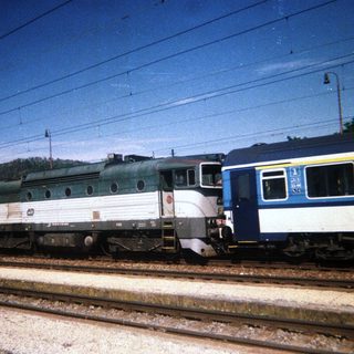 Green locomotive and blue train car sit on railway tracks.
